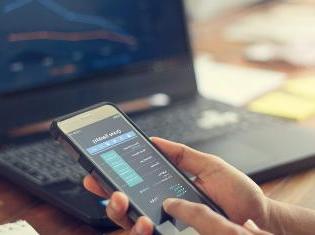 A person comparing financial stocks on a smart phone and a laptop.